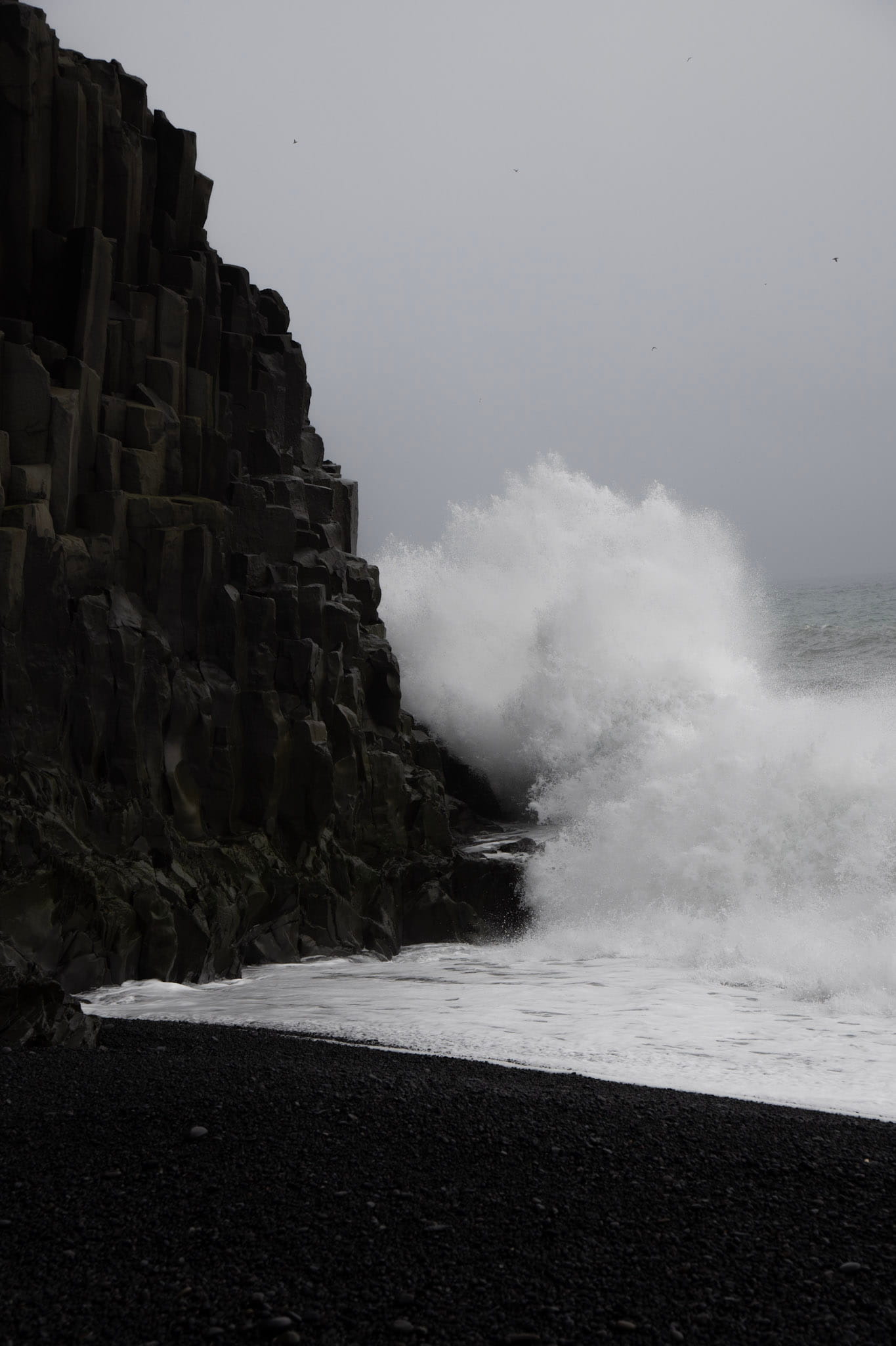 Ocean wave crashing into black basalt columns